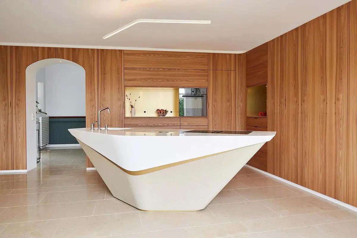 Îlot de cuisine facetté en solid surface blanc avec filet laiton, entouré de panneaux de bois